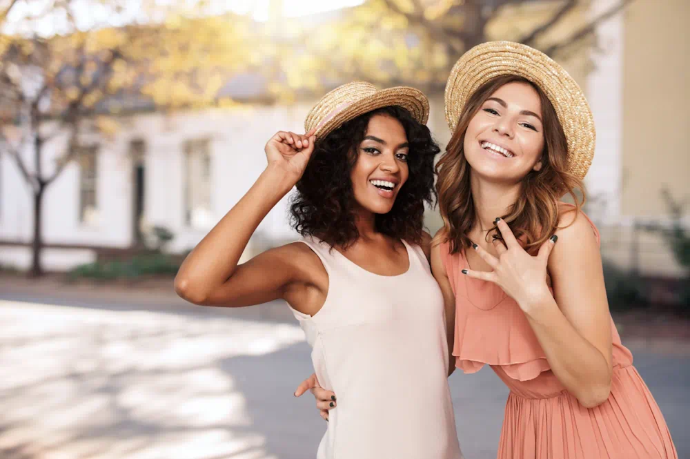 Two friends smiling outdoors in summer hats.